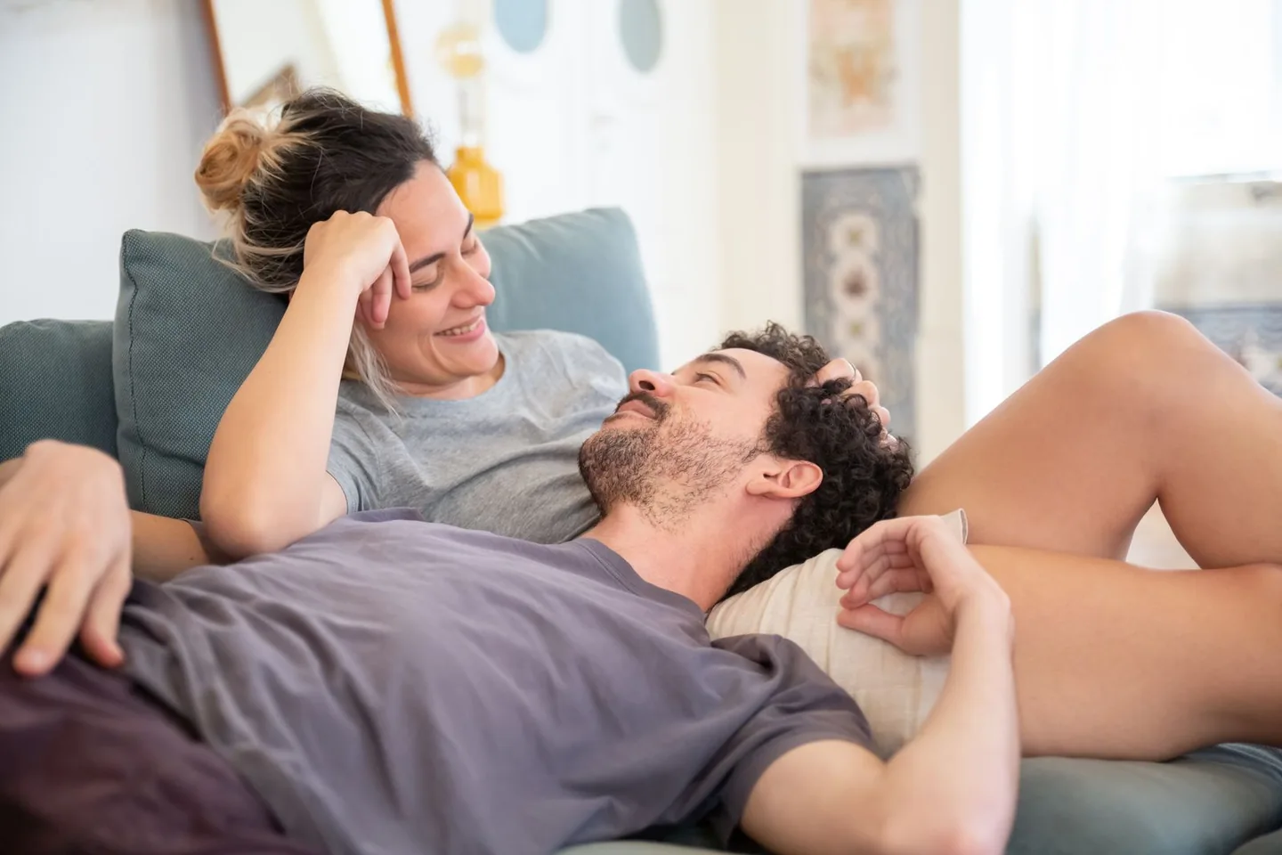 An adult couple relaxing on a sofa, the man resting his head on the smiling woman's lap